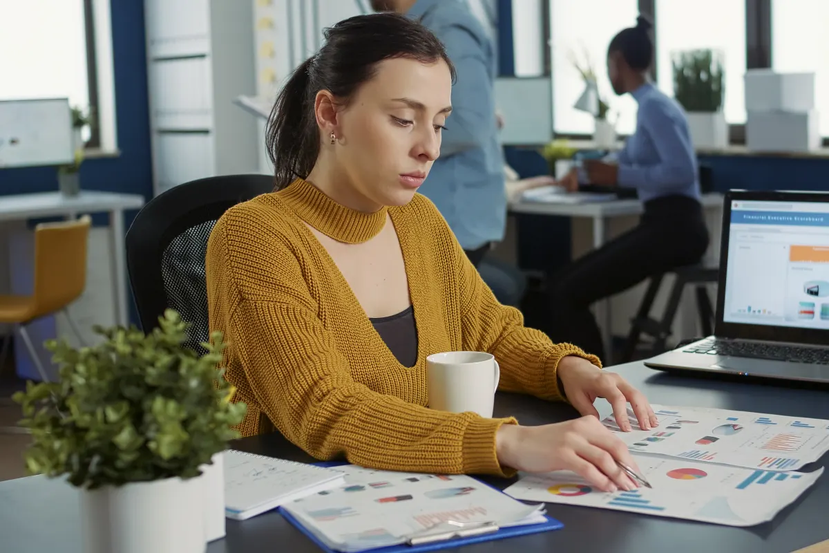 En kvinna jämför rapporter med diagram vid sitt skrivbord.
